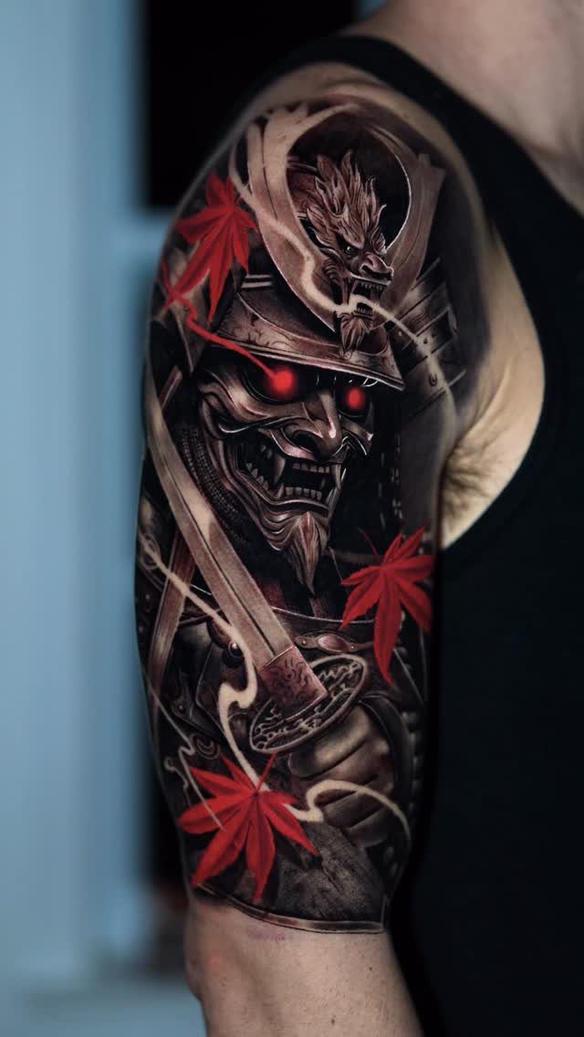 Samurai mask tattoo with red eyes and maple leaves on a man's arm.