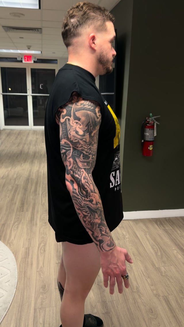 Man with a detailed black and grey full sleeve tattoo on his right arm.