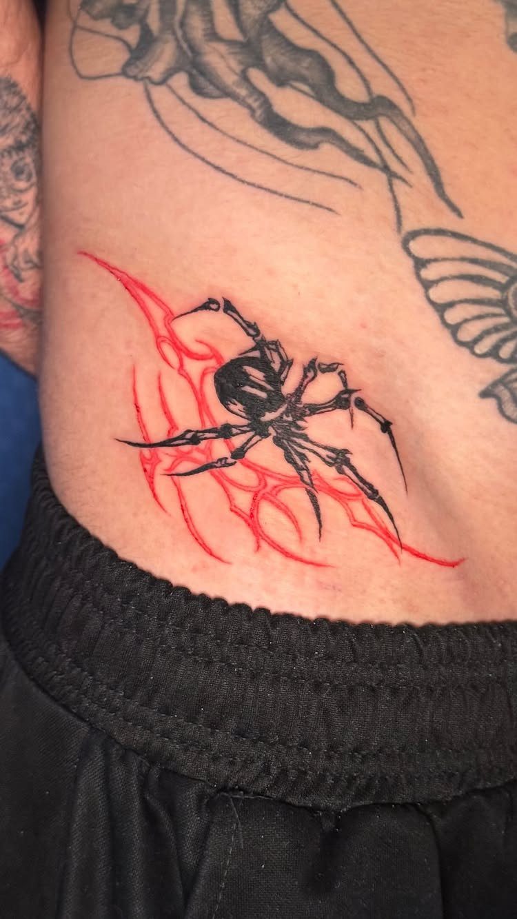 Black spider tattoo with red accents on a person's lower torso skin.