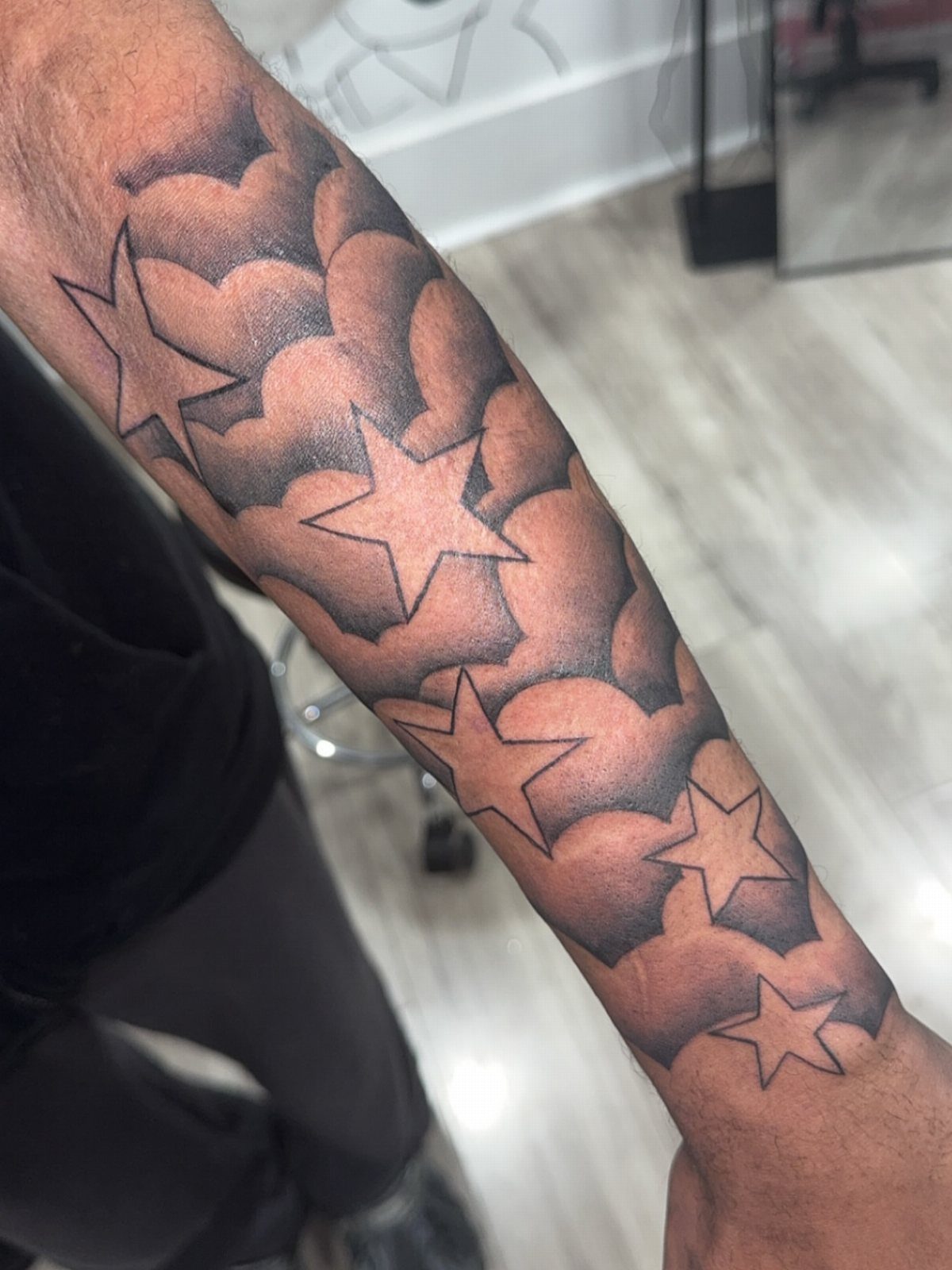 Tattoo of five-pointed stars and clouds on a man's forearm in black and grey ink.