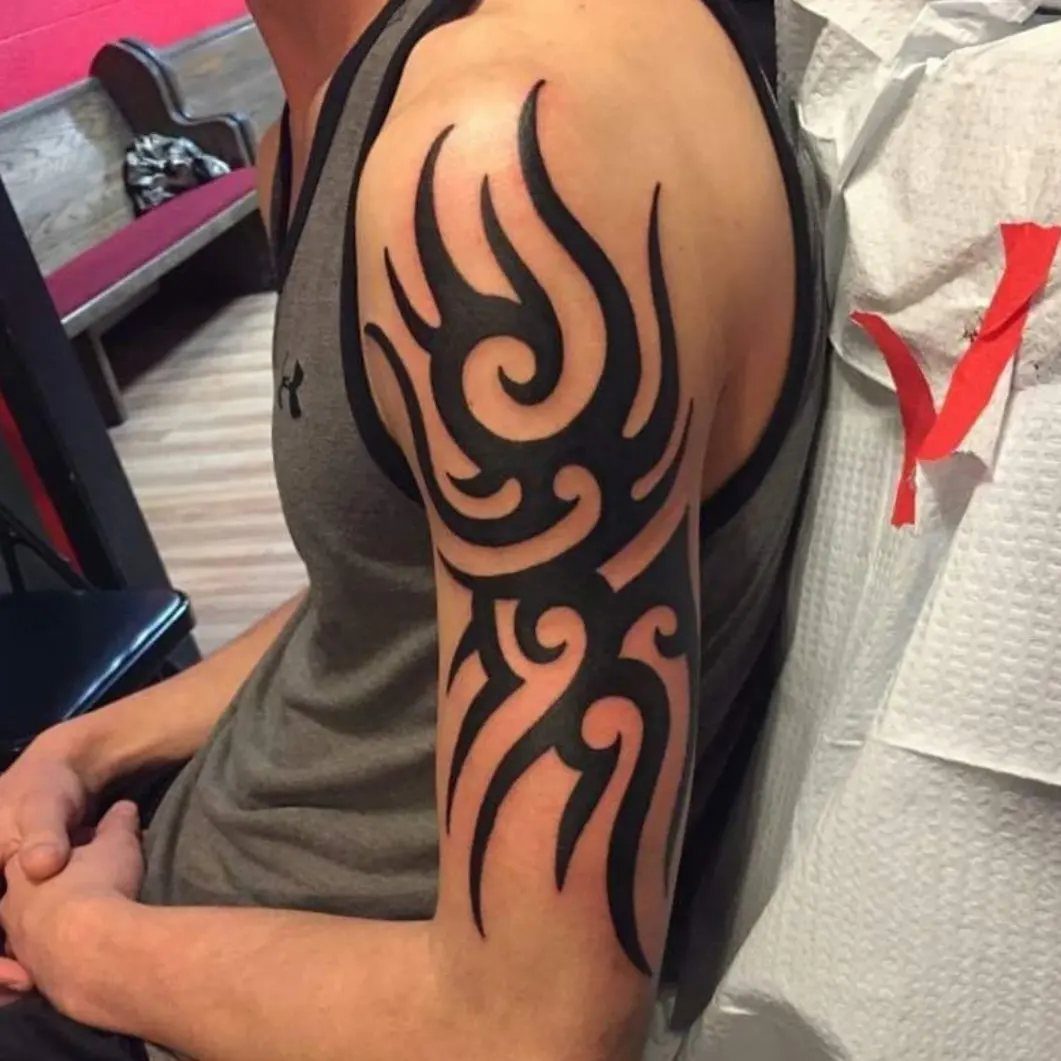 Bold black tribal tattoo with swirling patterns on a man's upper arm.