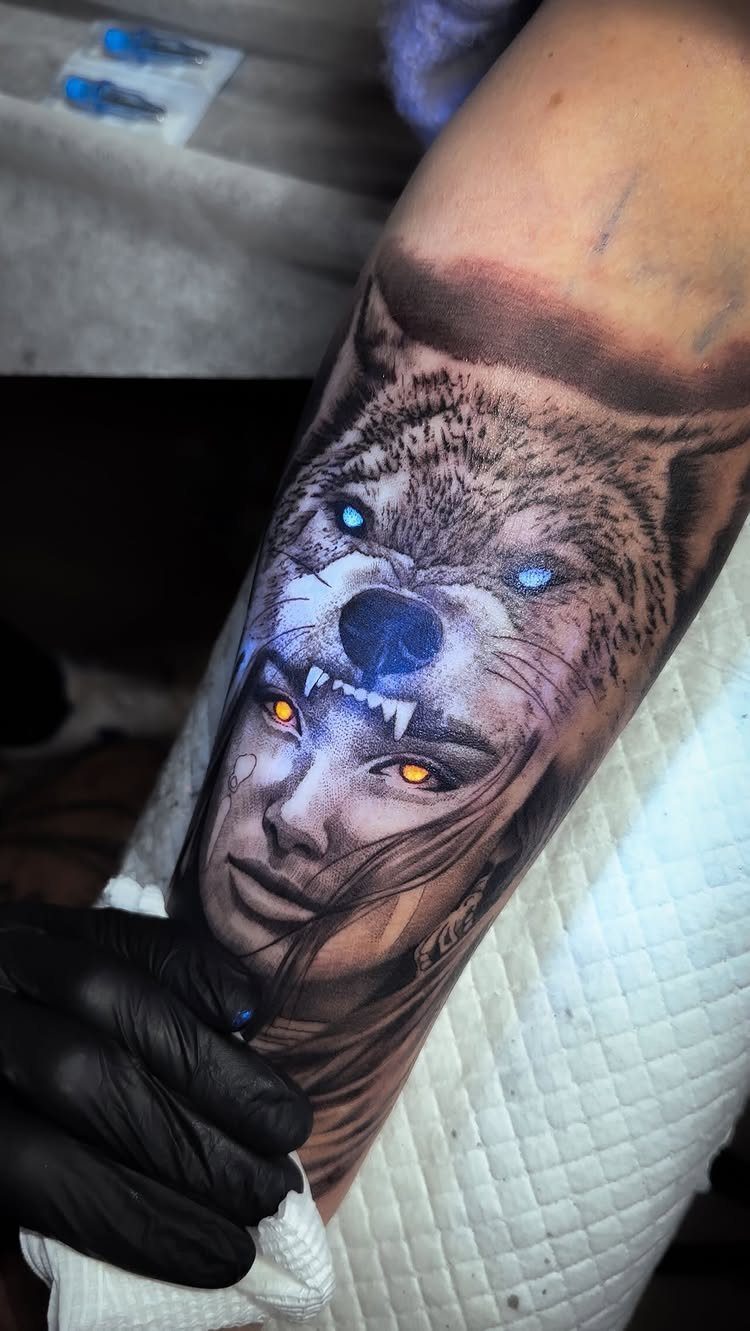 Wolf and woman face tattoo on an arm with glowing blue and orange eyes.