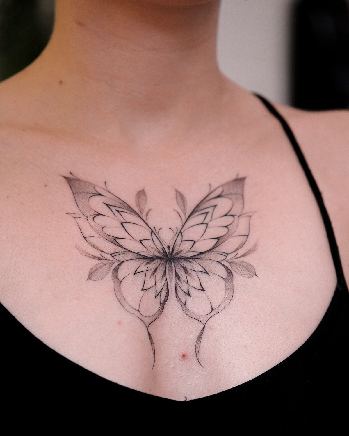 Stylized butterfly tattoo with floral details centered on a person's chest between breasts.