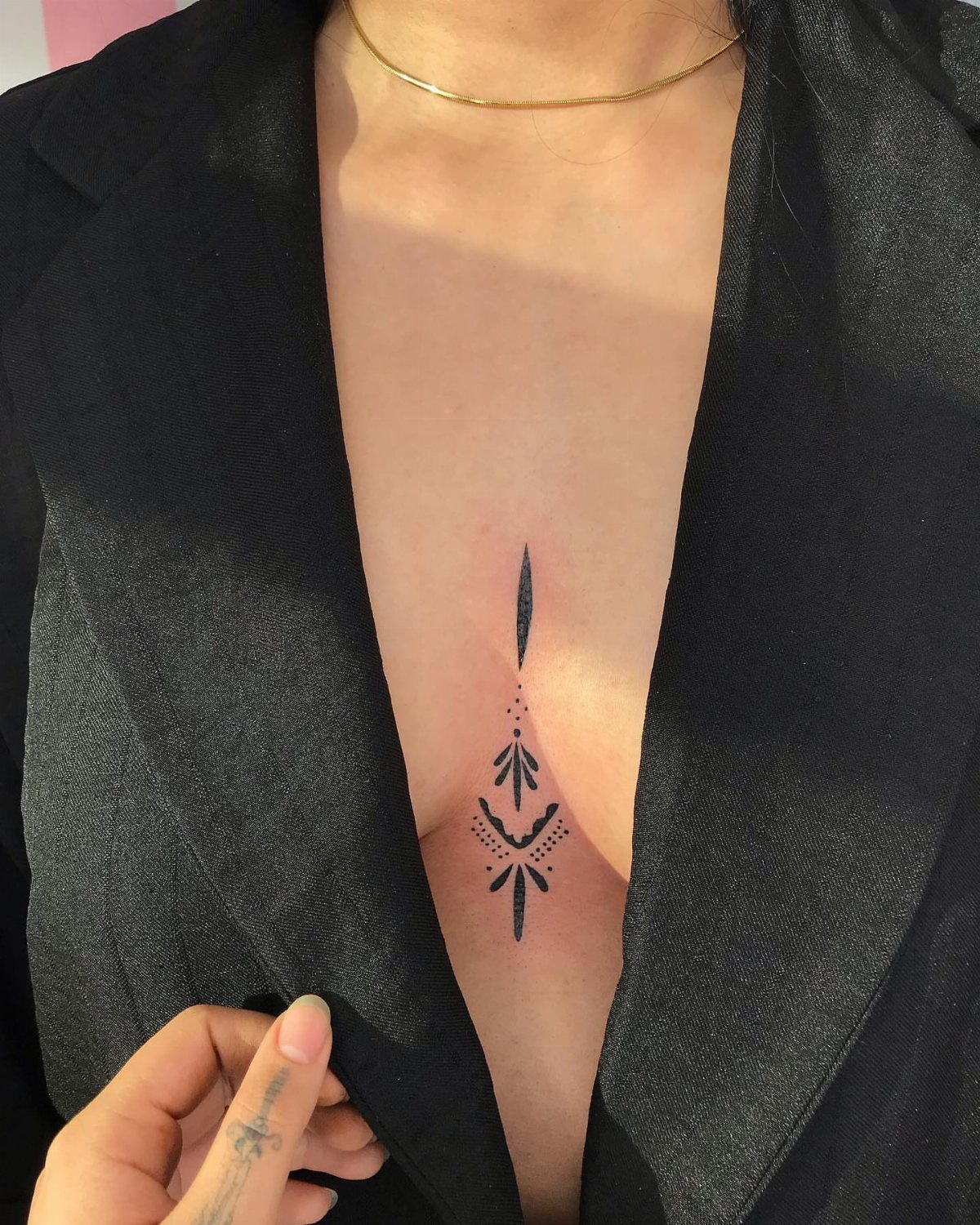 Geometric black ink tattoo centered on a person's chest between the breasts.
