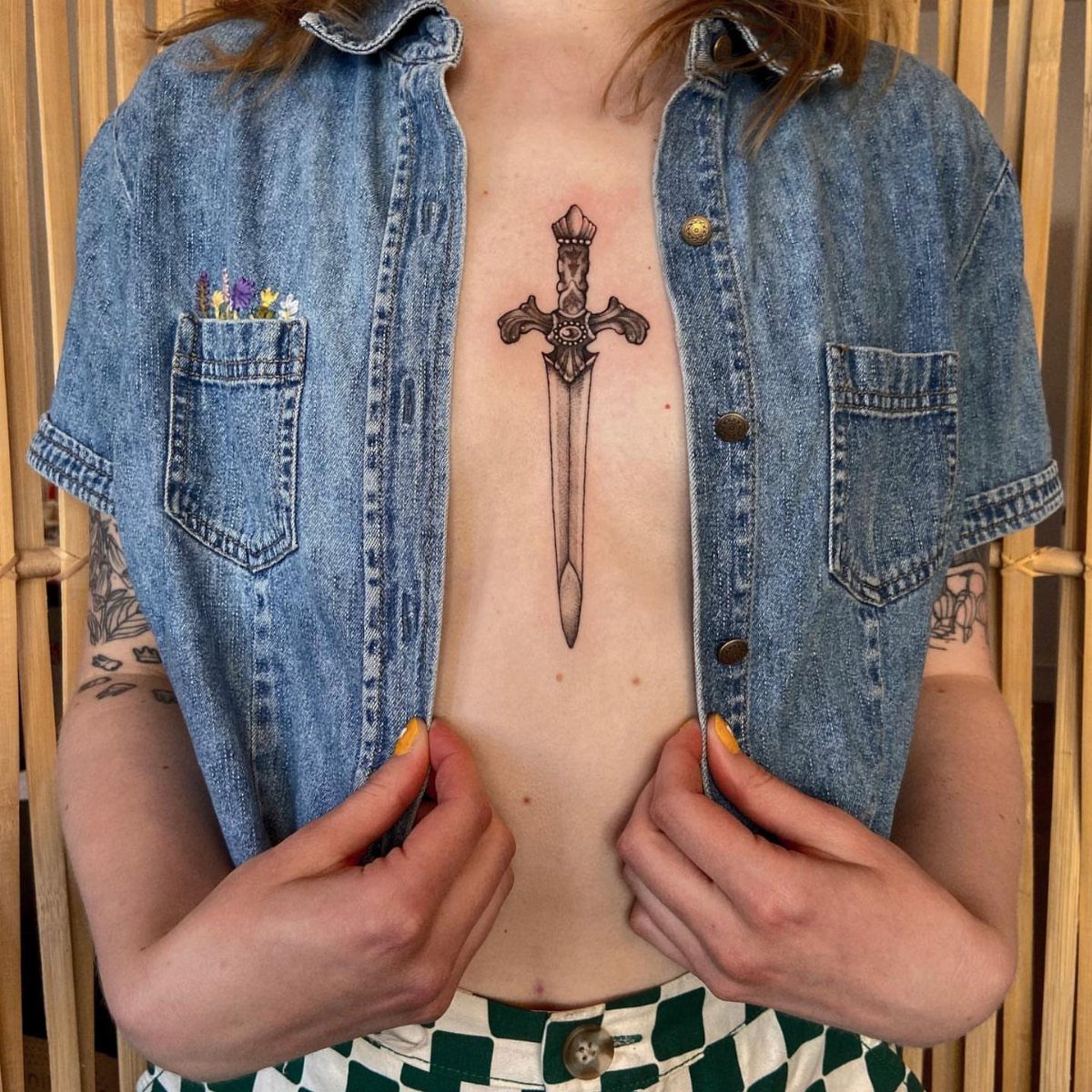 Dagger tattoo on the sternum of a person wearing an open denim vest.