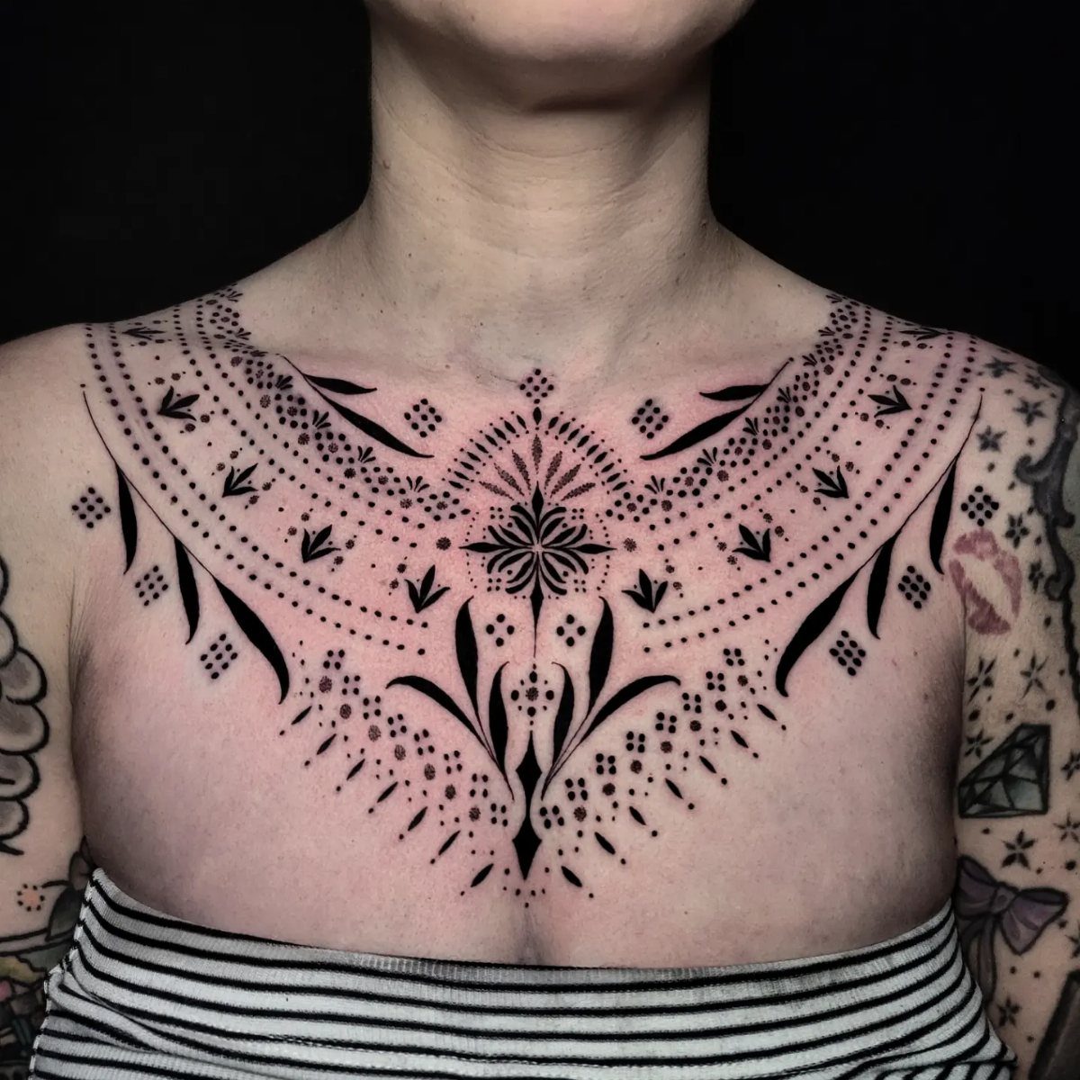 Symmetrical black ink dotwork tattoo on a person's chest between the breasts.