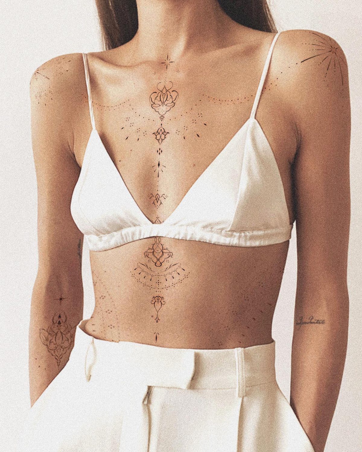 Woman with fine line ornamental tattoos running vertically down her sternum and abdomen.