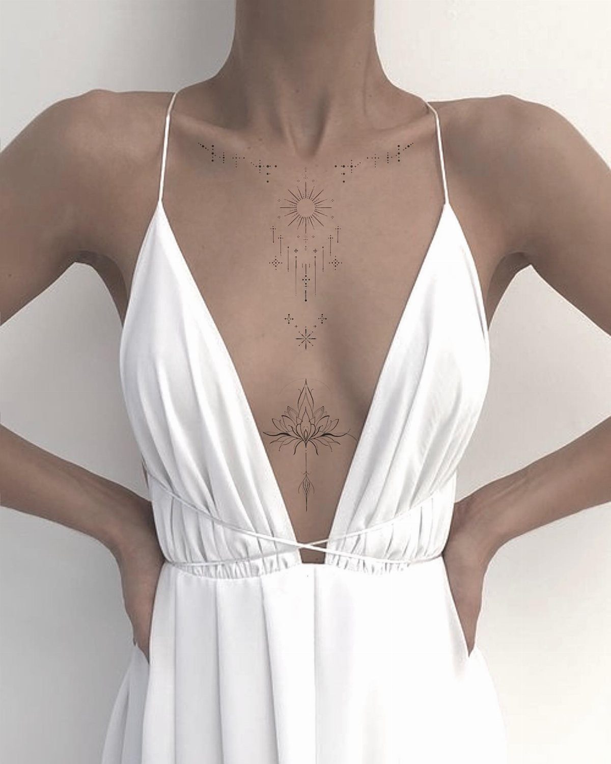 Lotus flower and sun tattoos on a woman's sternum and chest area.