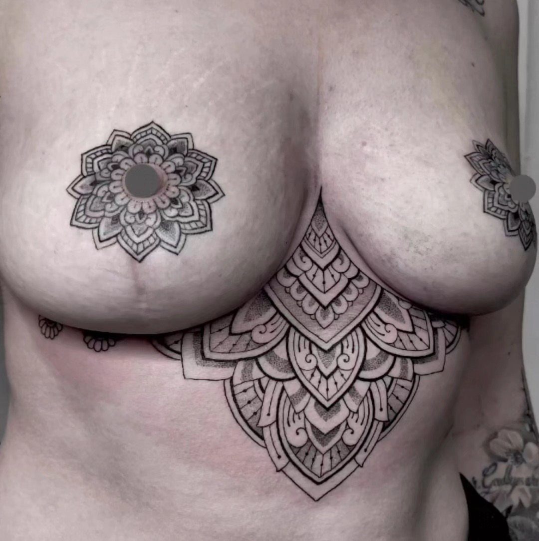 Intricate black ink mandala tattoos on the sternum and nipples of a chest.