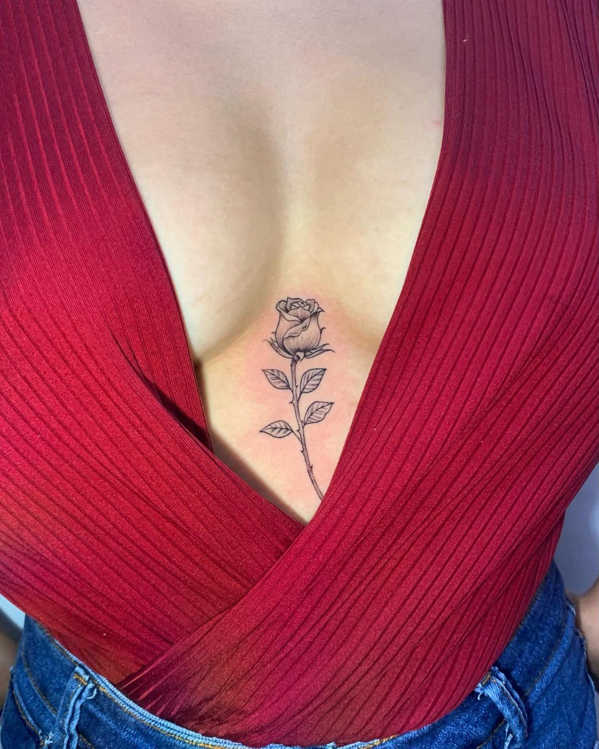 Rose tattoo with stem and leaves located on the sternum between breasts