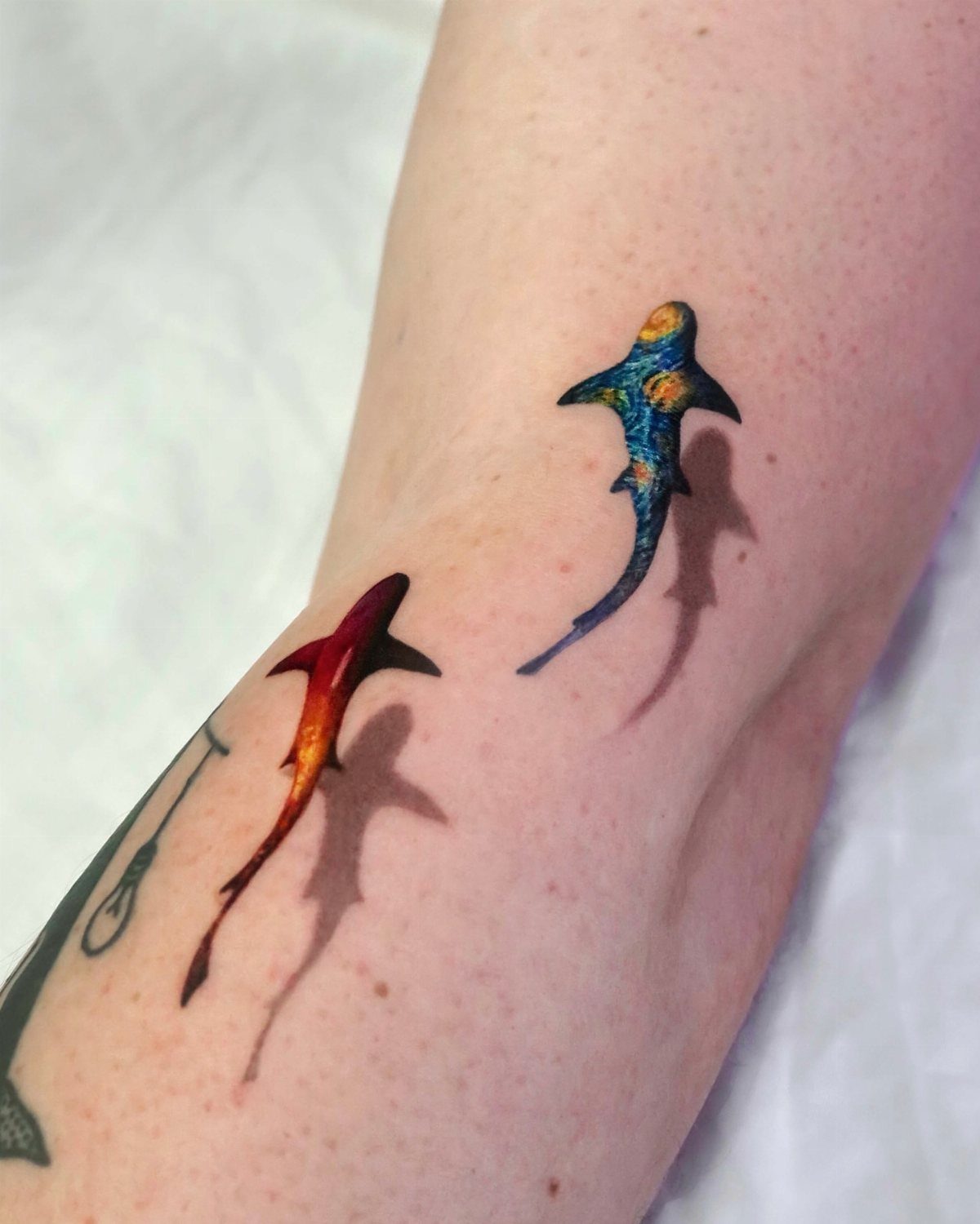 Two colorful shark tattoos with drop shadows creating a 3D effect on an arm.