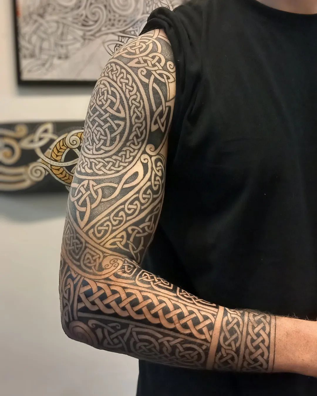 Man's arm with a full sleeve Celtic knotwork tattoo in black and grey ink.