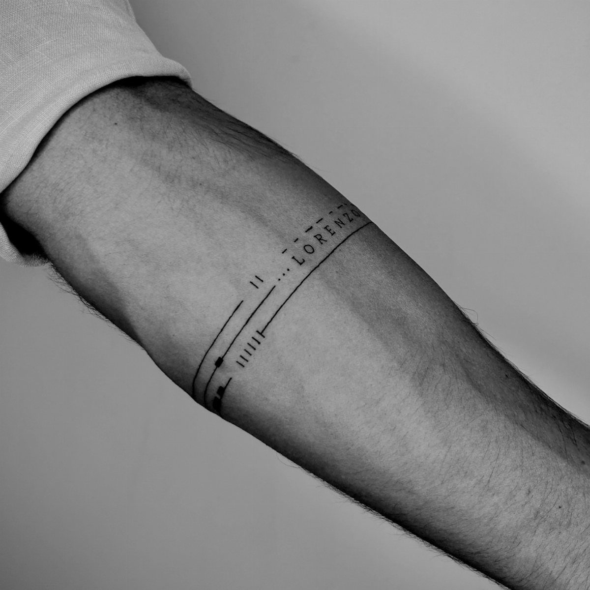 Man's forearm with a minimalist black line armband tattoo including the name Lorenzo.