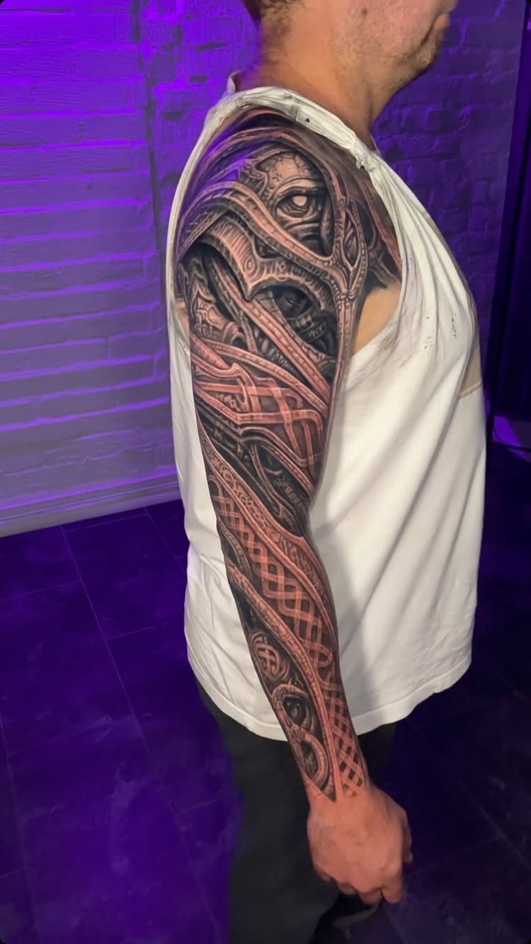 Biomechanical sleeve tattoo on a man's arm featuring metallic and organic mechanical elements.