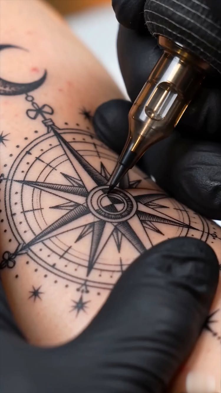 Compass tattoo being inked on skin by a tattoo artist using a machine.