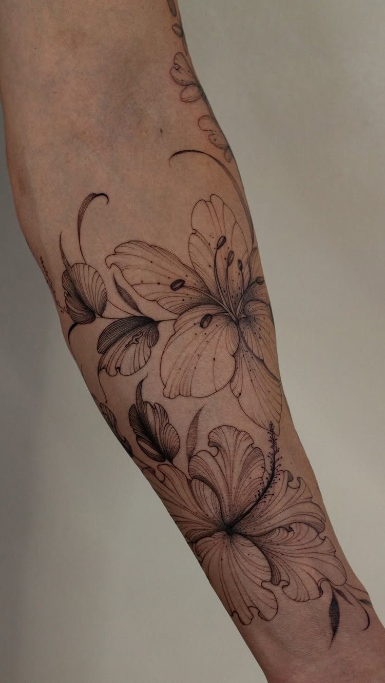 Floral tattoos of lilies and leaves on a person's forearm in black ink.