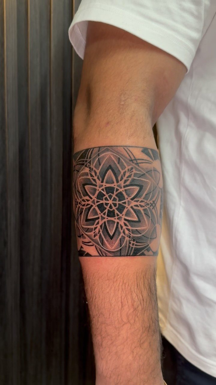 Geometric mandala tattoo wrapping around a man's upper arm as a bold armband.
