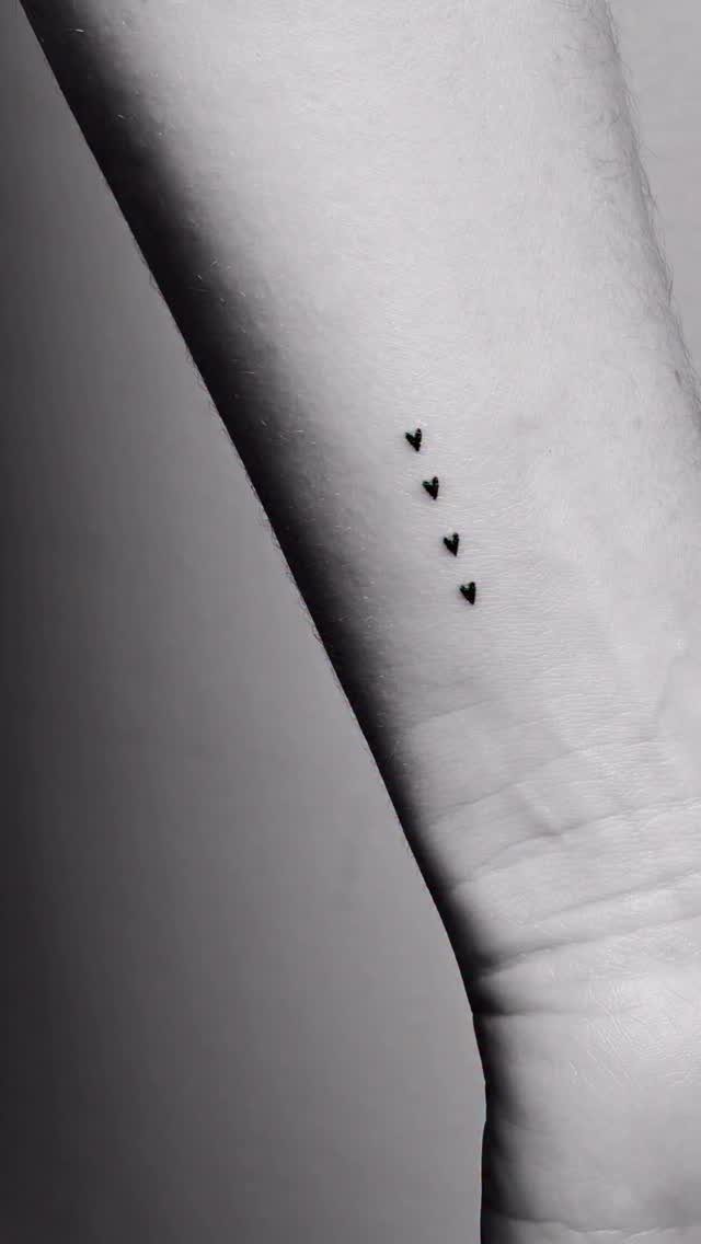 Four small black heart tattoos aligned vertically on a person's forearm.