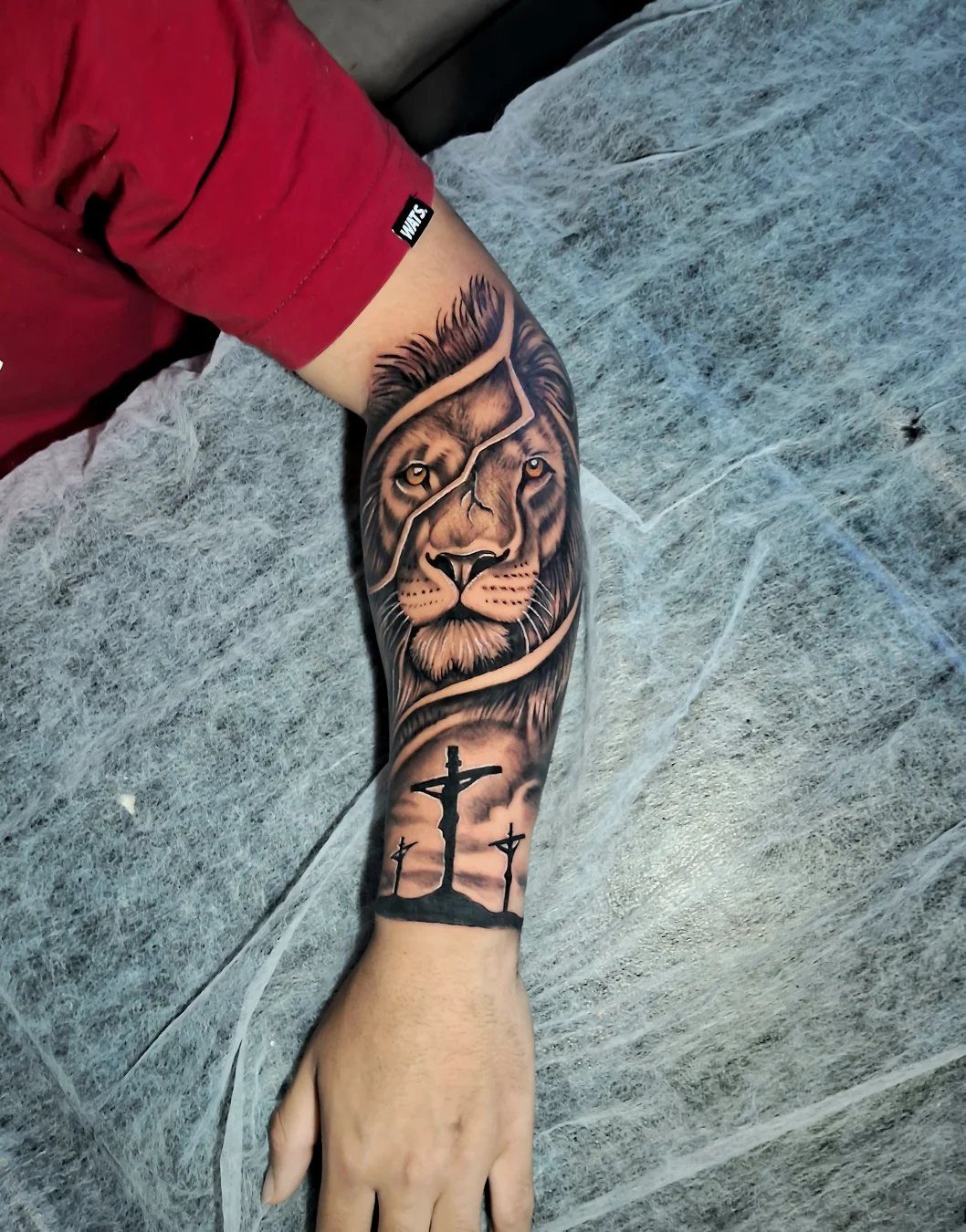 Lion and three crosses tattoo on a man's forearm over white background