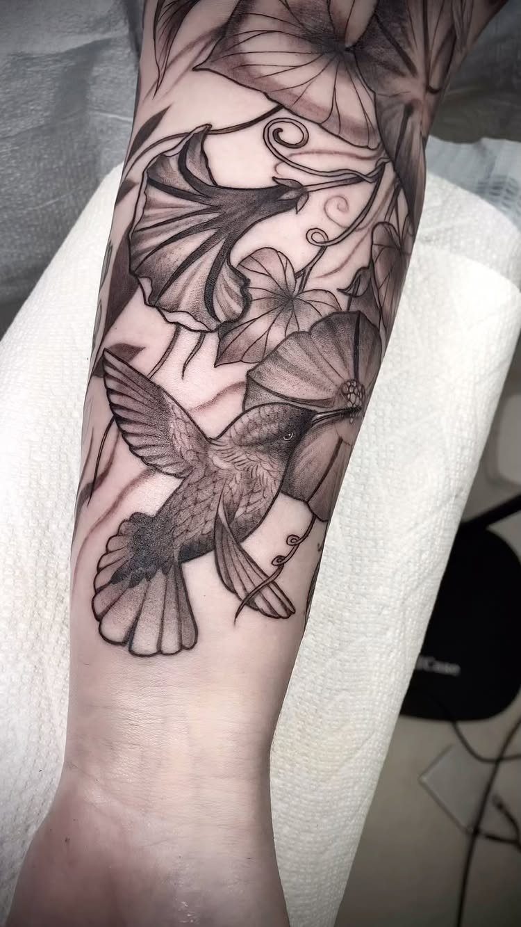 Hummingbird and floral tattoo in black and grey ink on a person's forearm