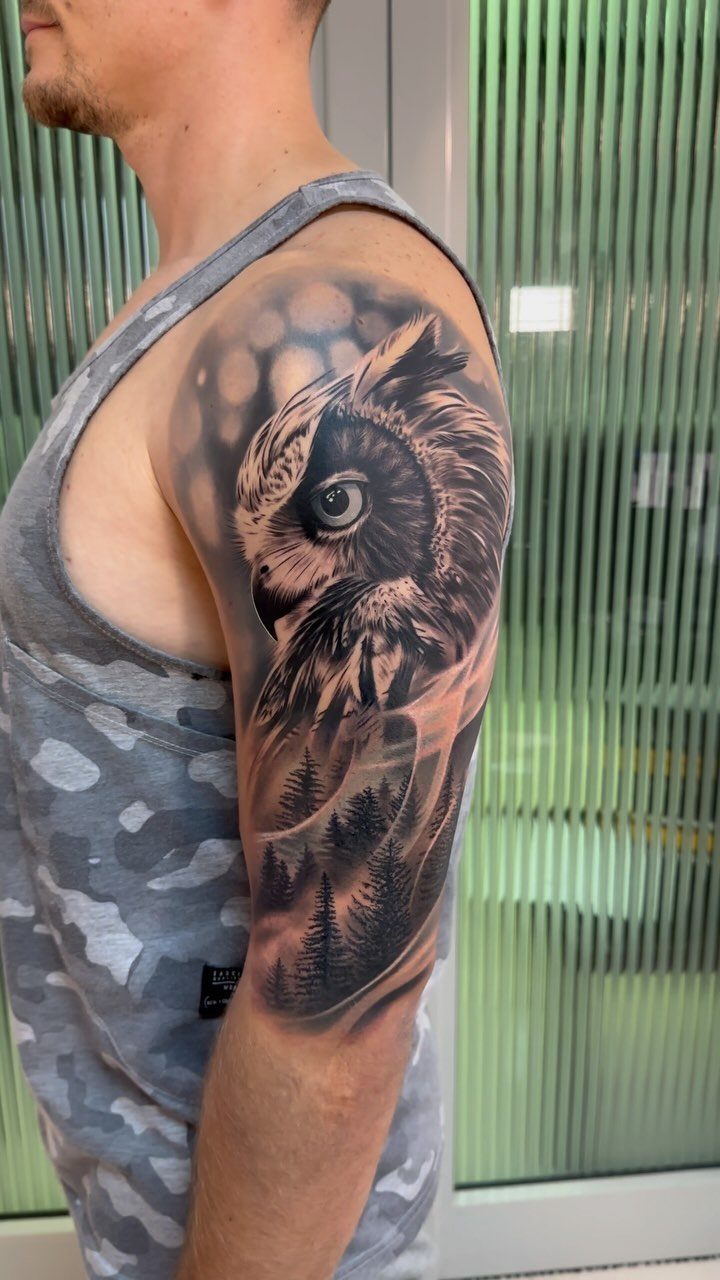 Owl tattoo with a pine forest on a man's upper arm