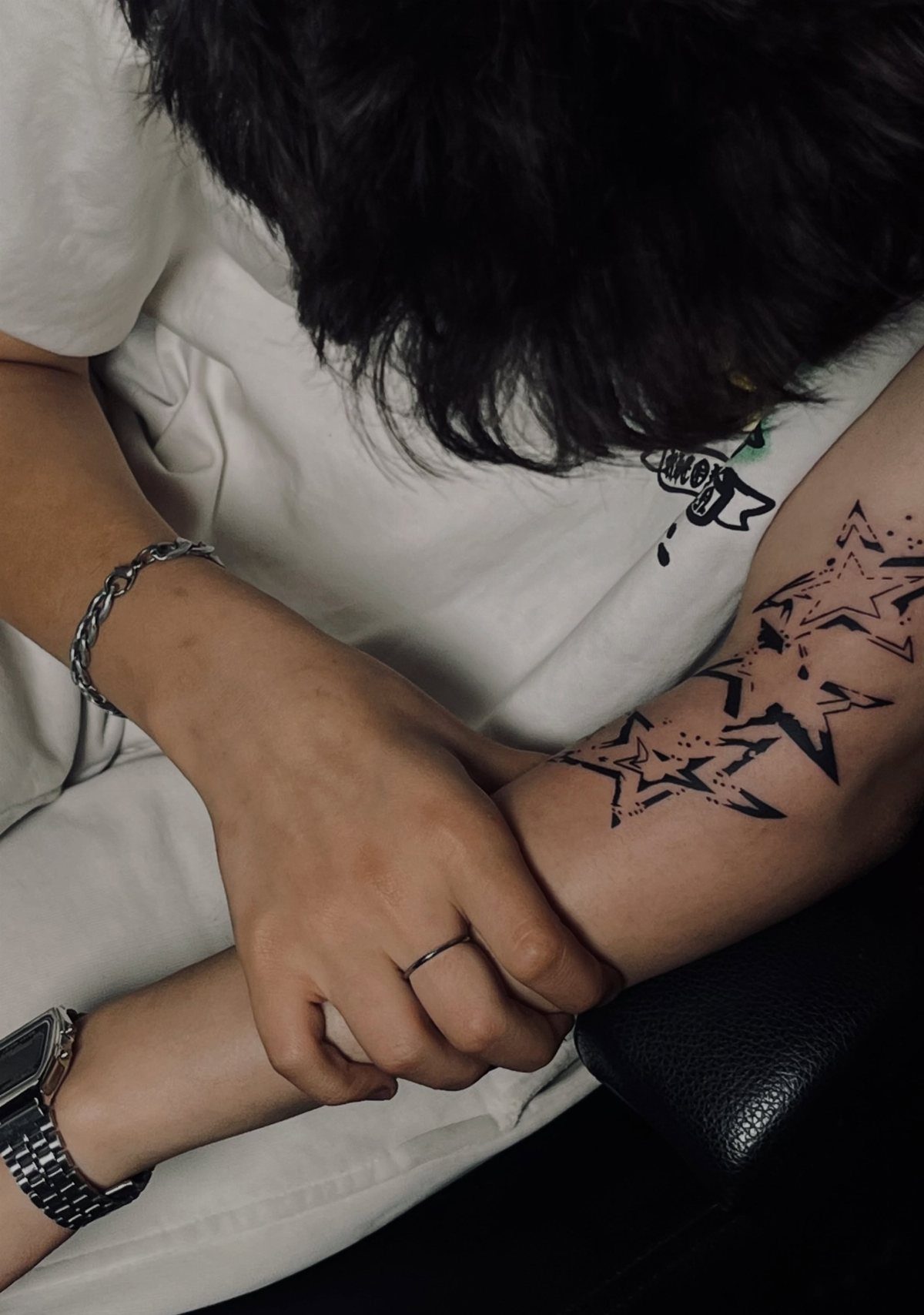 Black ink star tattoos on a person's forearm with silver jewelry and white clothing.
