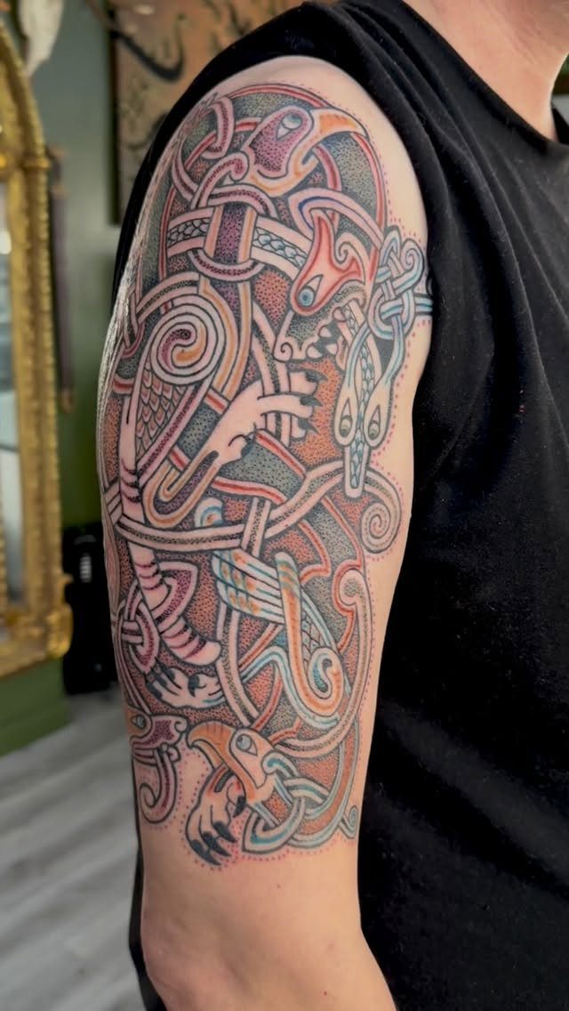 Intricate Celtic knot tattoo with colorful animals on a man's upper arm.