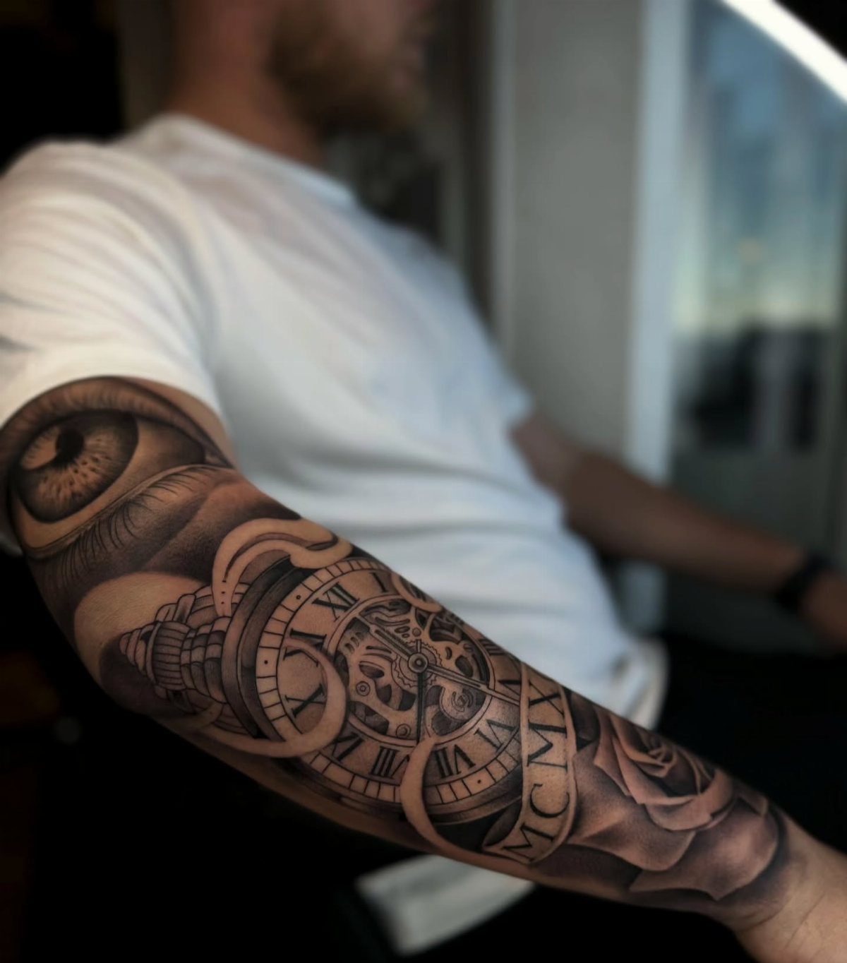 Detailed black and grey forearm tattoo featuring a pocket watch, eye, and rose.