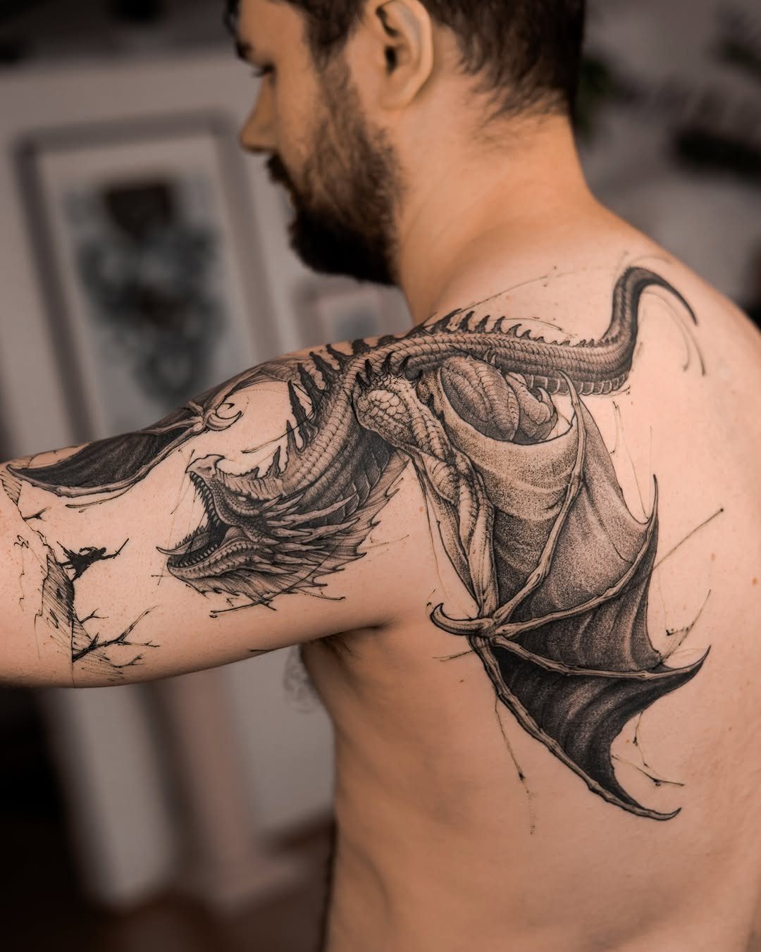 Detailed black and grey dragon tattoo on a man's shoulder and upper arm.