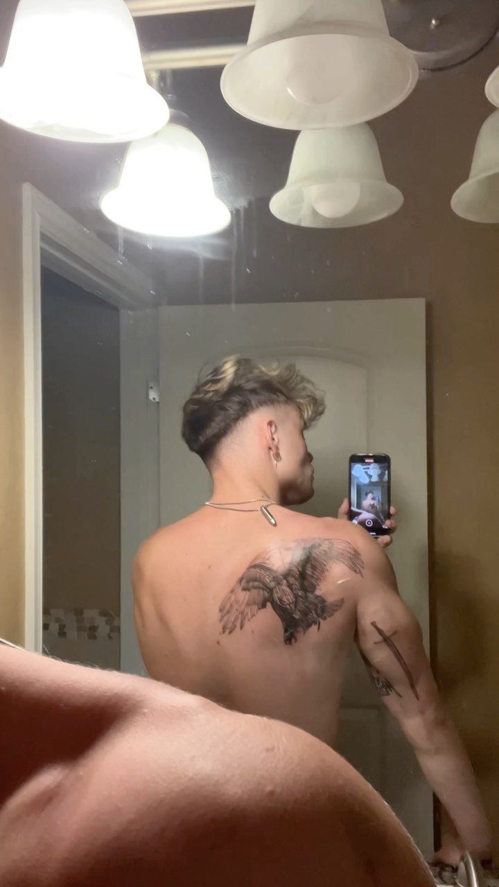 Man with a large eagle tattoo on his upper back taking a mirror selfie.