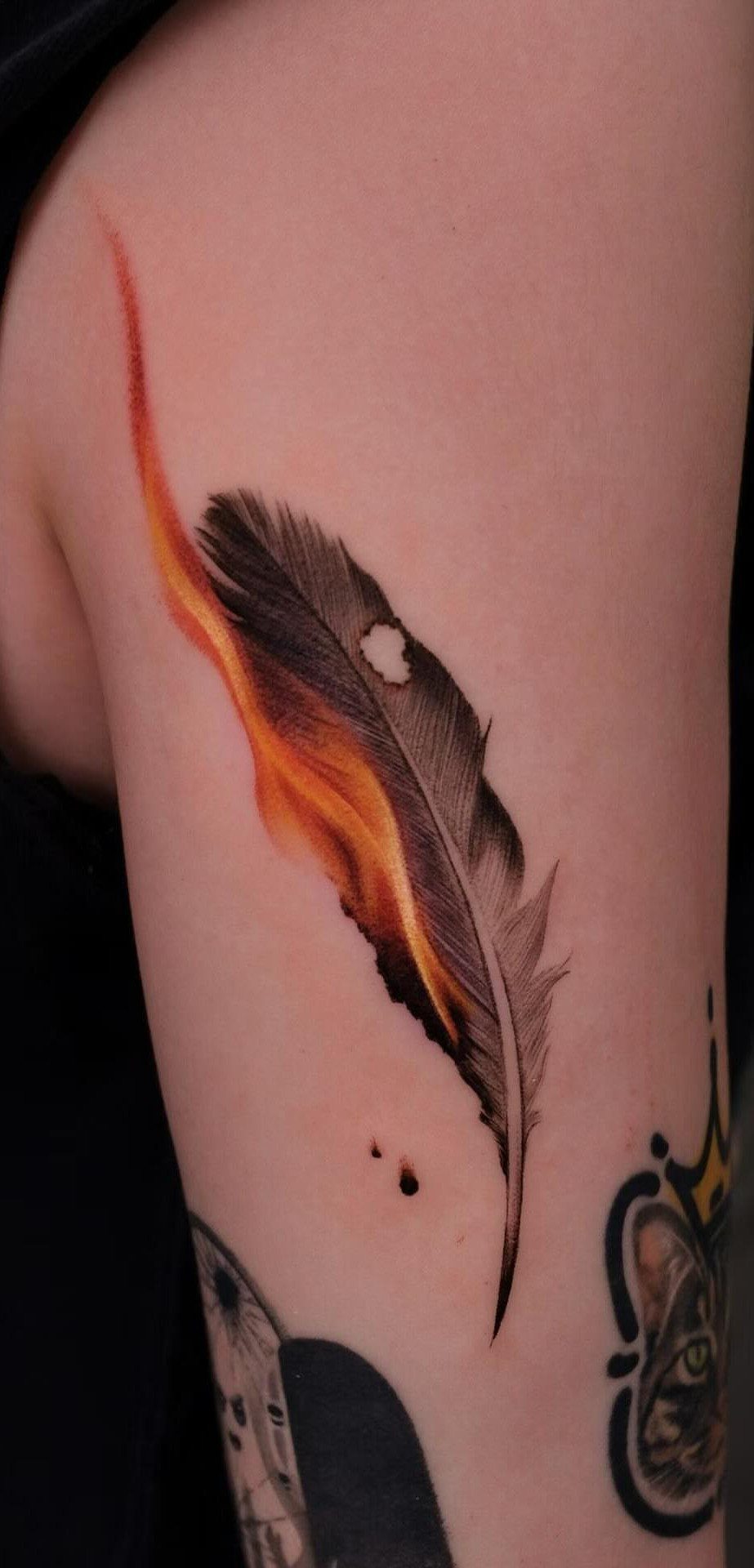 Feather tattoo on an arm with one side appearing as orange and red flames.