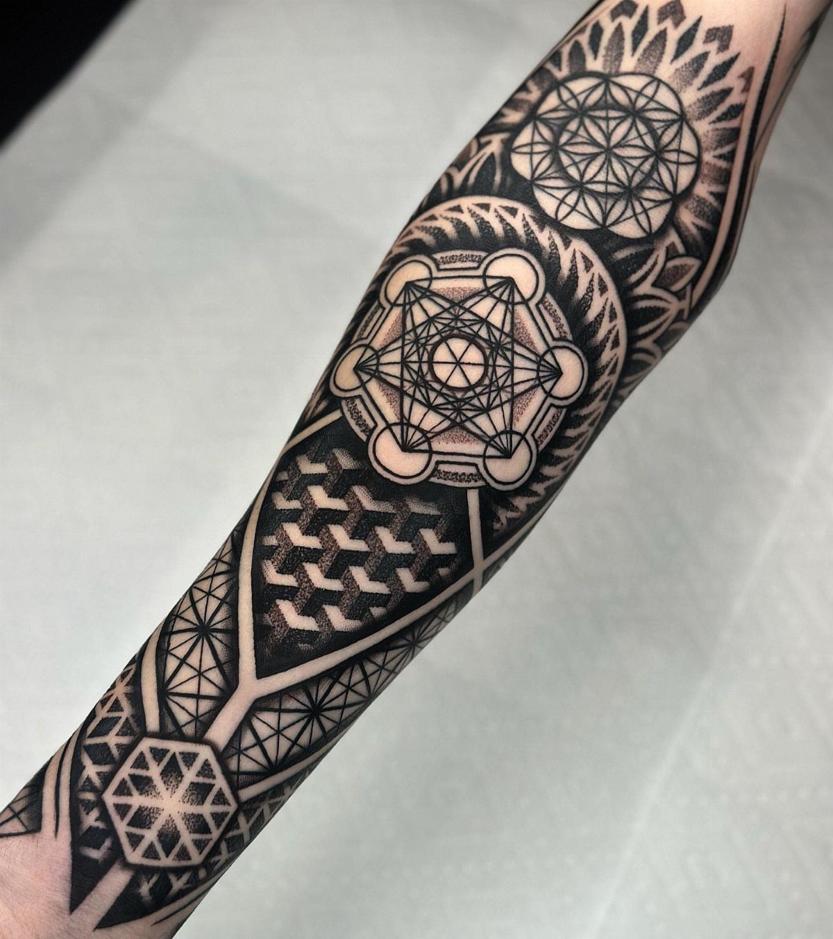 Forearm with a detailed black ink geometric tattoo featuring complex interlocking shapes.