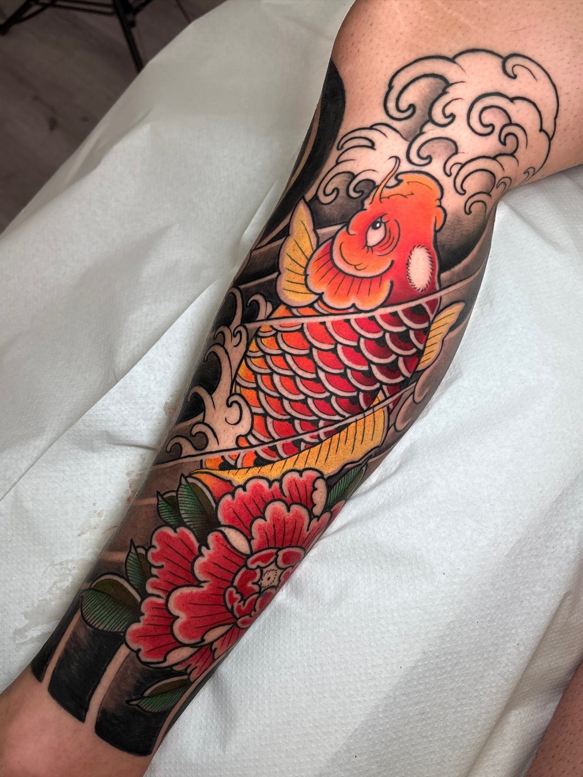 Koi fish tattoo with red peony and stylized waves on a forearm