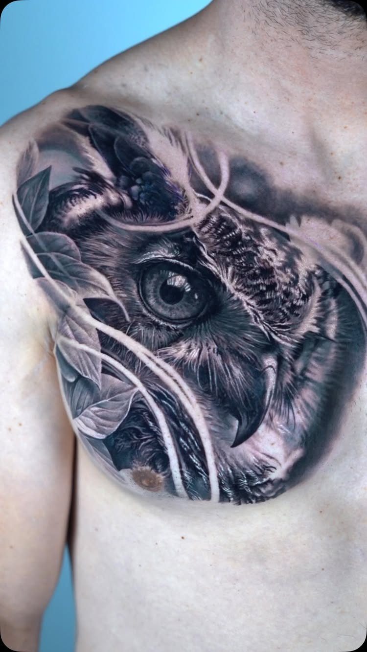Detailed black and grey owl tattoo on a man's chest and shoulder.
