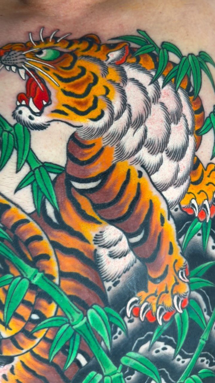 Roaring tiger tattoo with orange stripes and green bamboo leaves on skin.