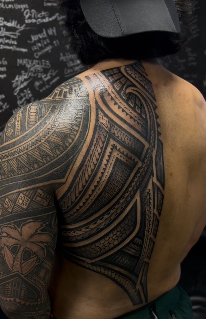 Large black tribal tattoo with geometric patterns on a man's shoulder and back.