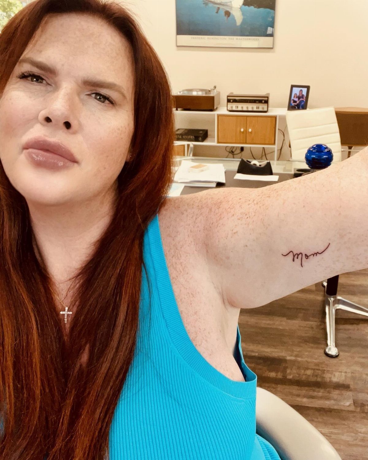 Woman with red hair showing a cursive Mom tattoo on her inner arm.