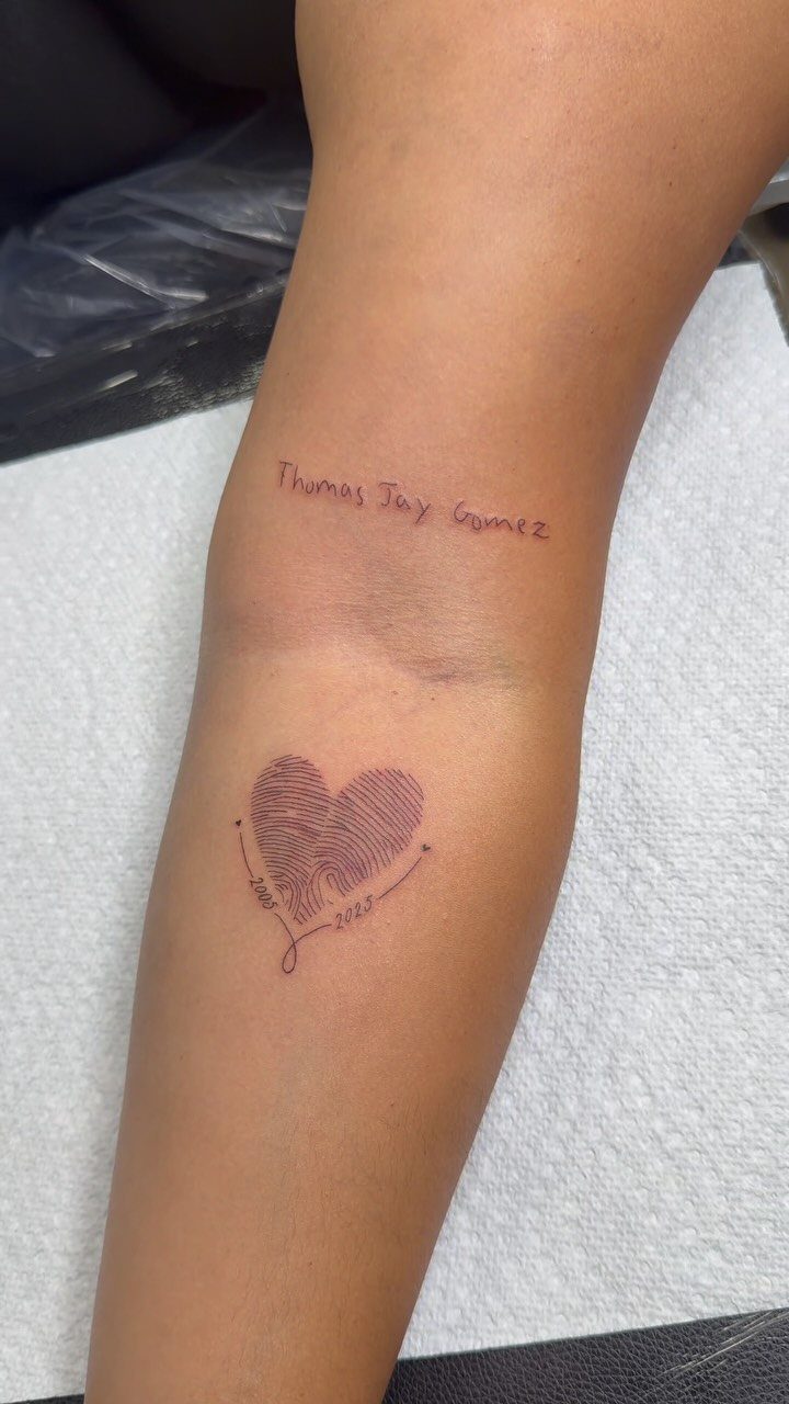 Heart-shaped fingerprint tattoo on a forearm with a name written in ink above.