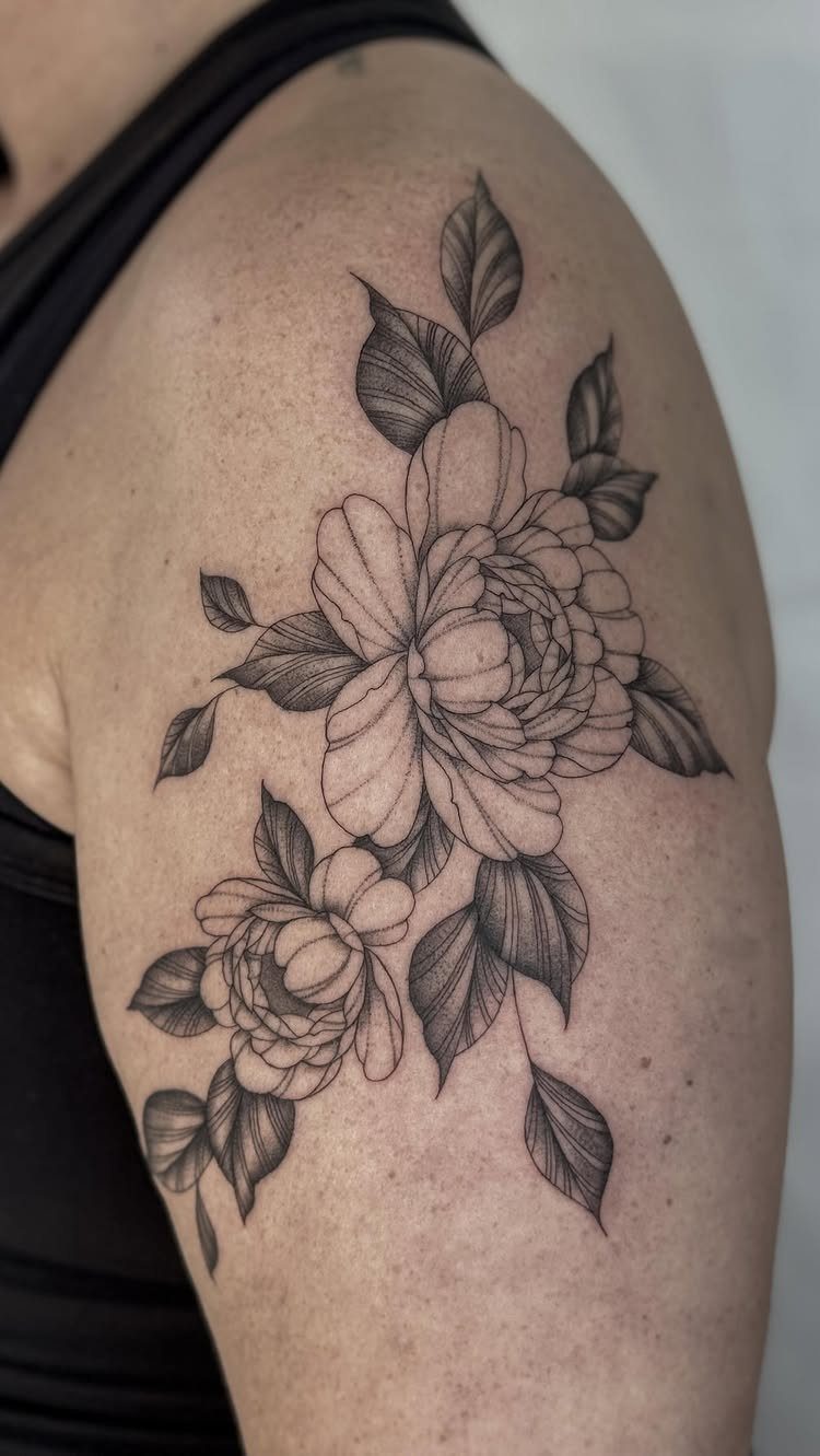 Floral peony tattoo with detailed leaves on a person's upper arm.