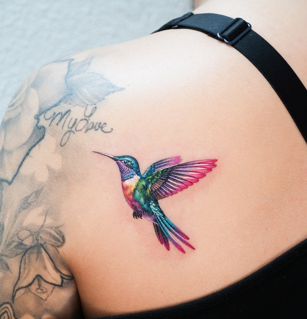Colorful hummingbird tattoo with pink and blue feathers on a person's shoulder.