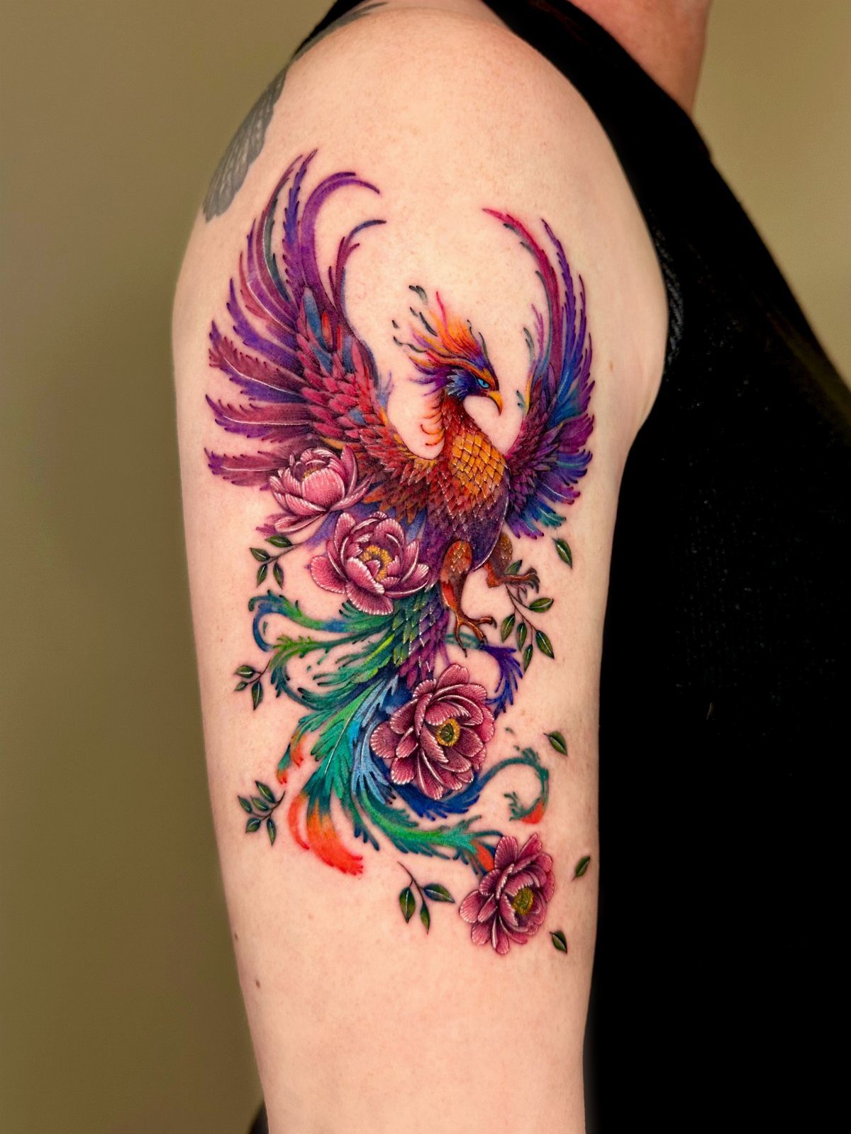 Colorful phoenix tattoo with pink flowers on a person's upper arm.
