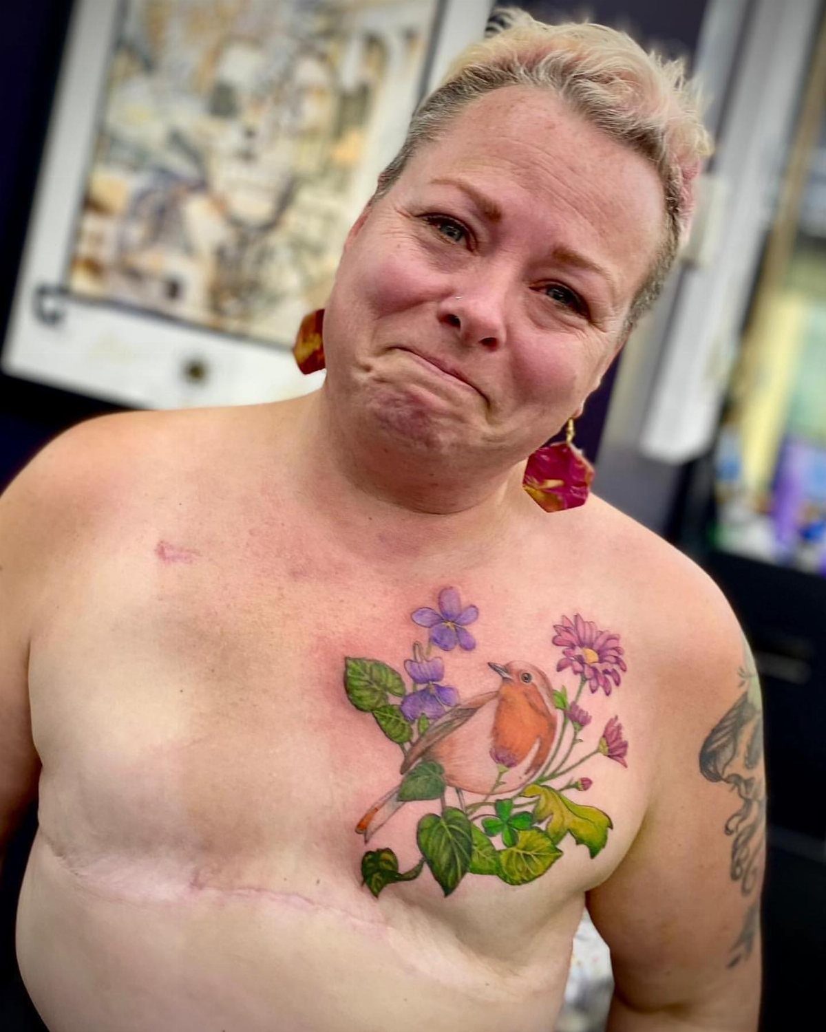 Woman with a colorful robin and flower tattoo placed near a chest scar.