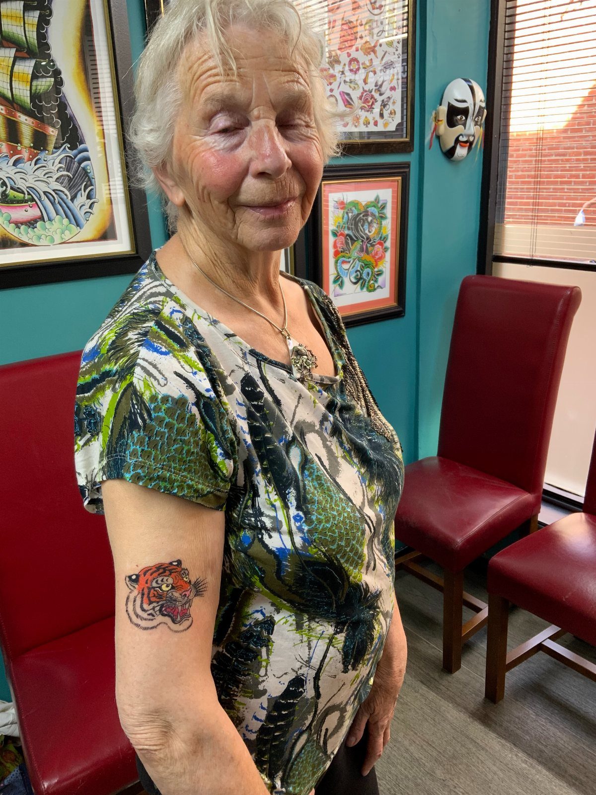 Older woman with white hair showing a colorful tiger tattoo on her arm.