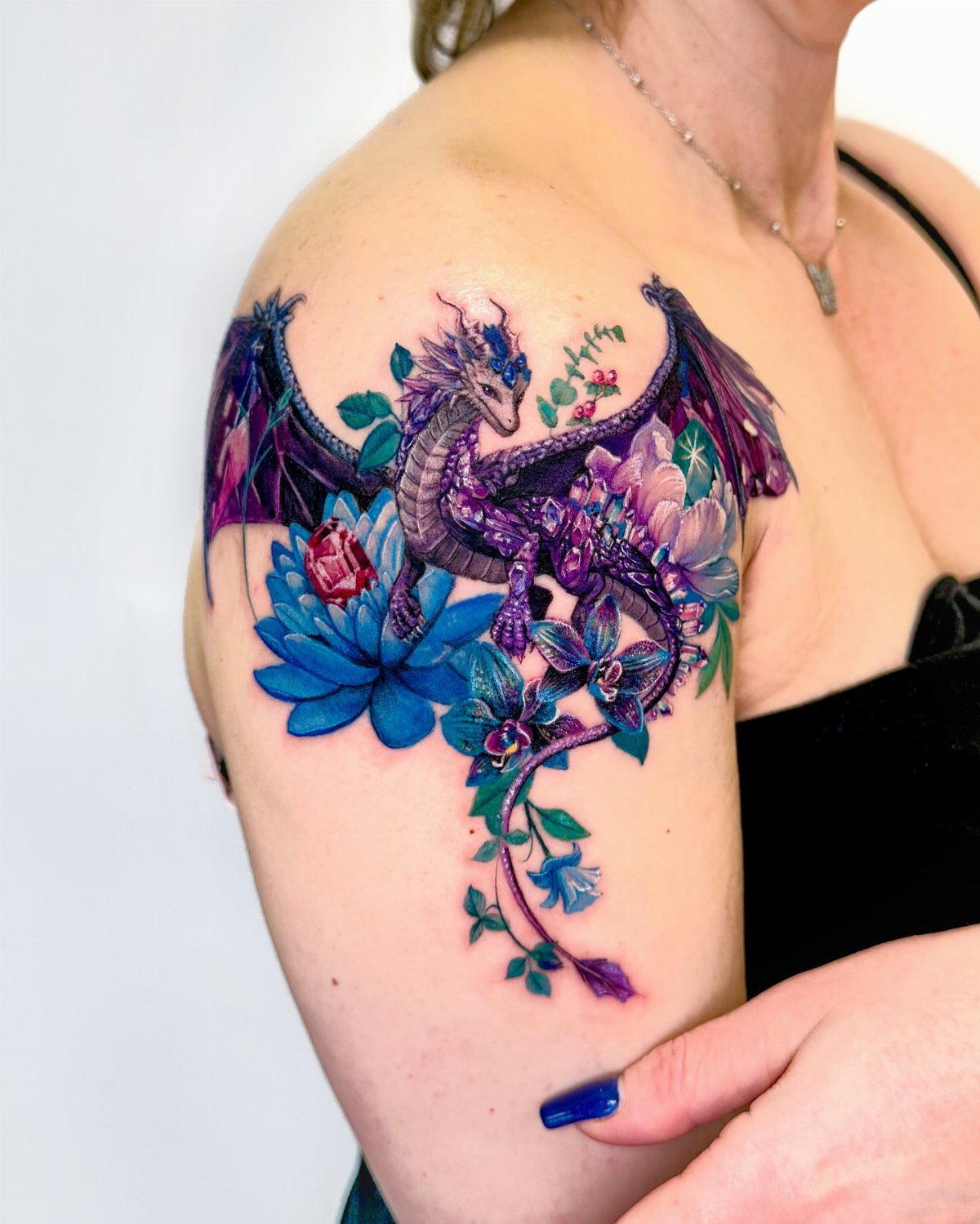 Purple dragon tattoo with blue flowers on a woman's upper arm