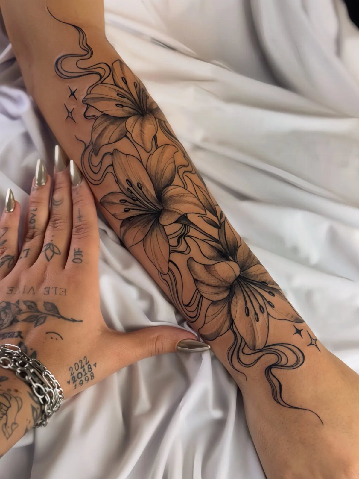 Floral half sleeve tattoo of lilies on a person's arm against white fabric.