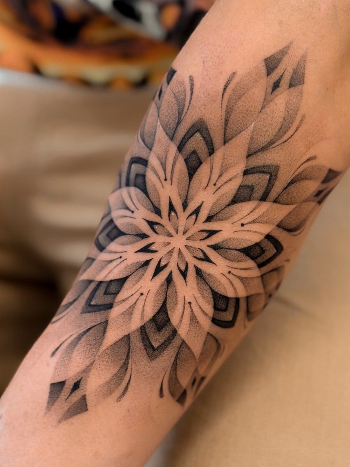 Symmetrical mandala tattoo in black and grey ink on a person's forearm.