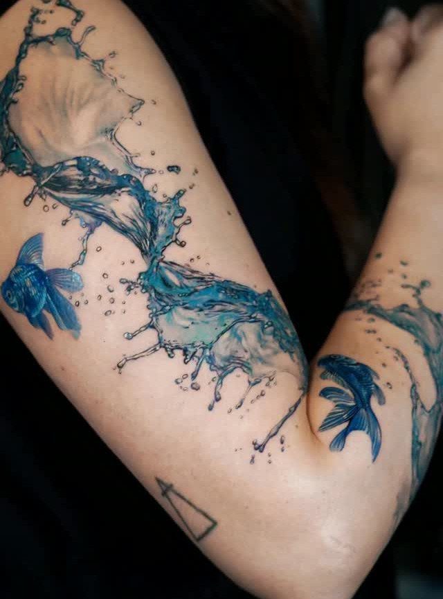 Watercolor half sleeve tattoo of blue splashing water and two betta fish.