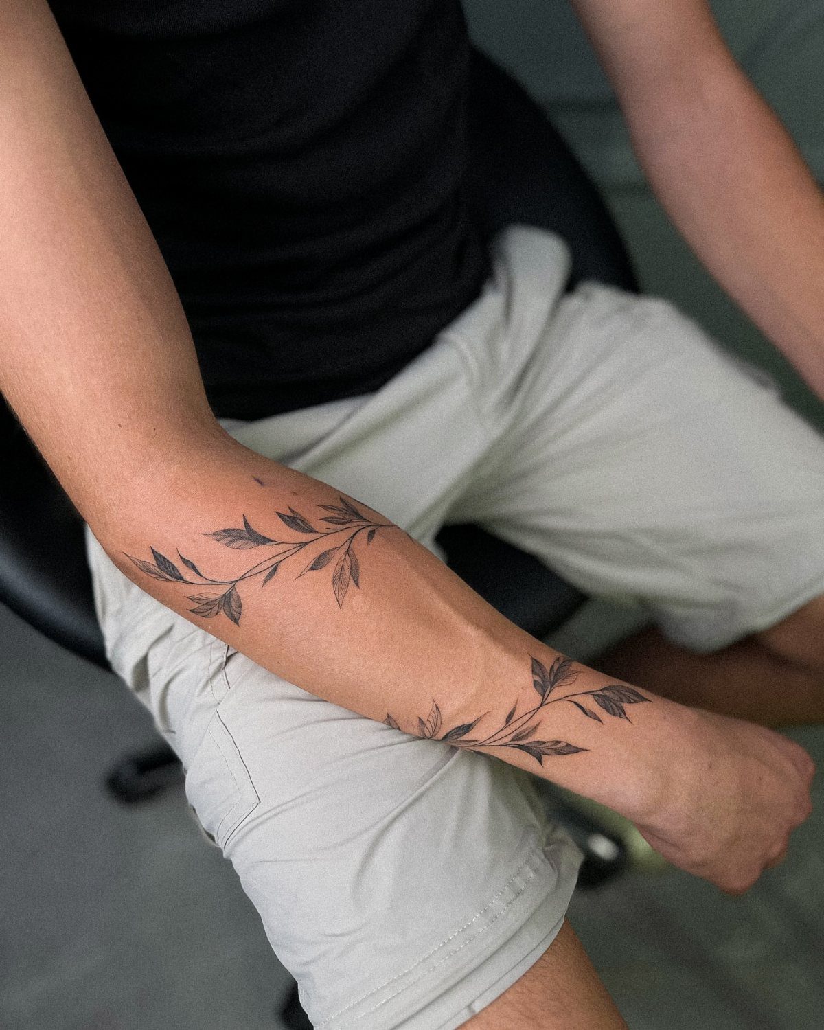 Man's forearm with black ink tattoos of leafy branches and stems.