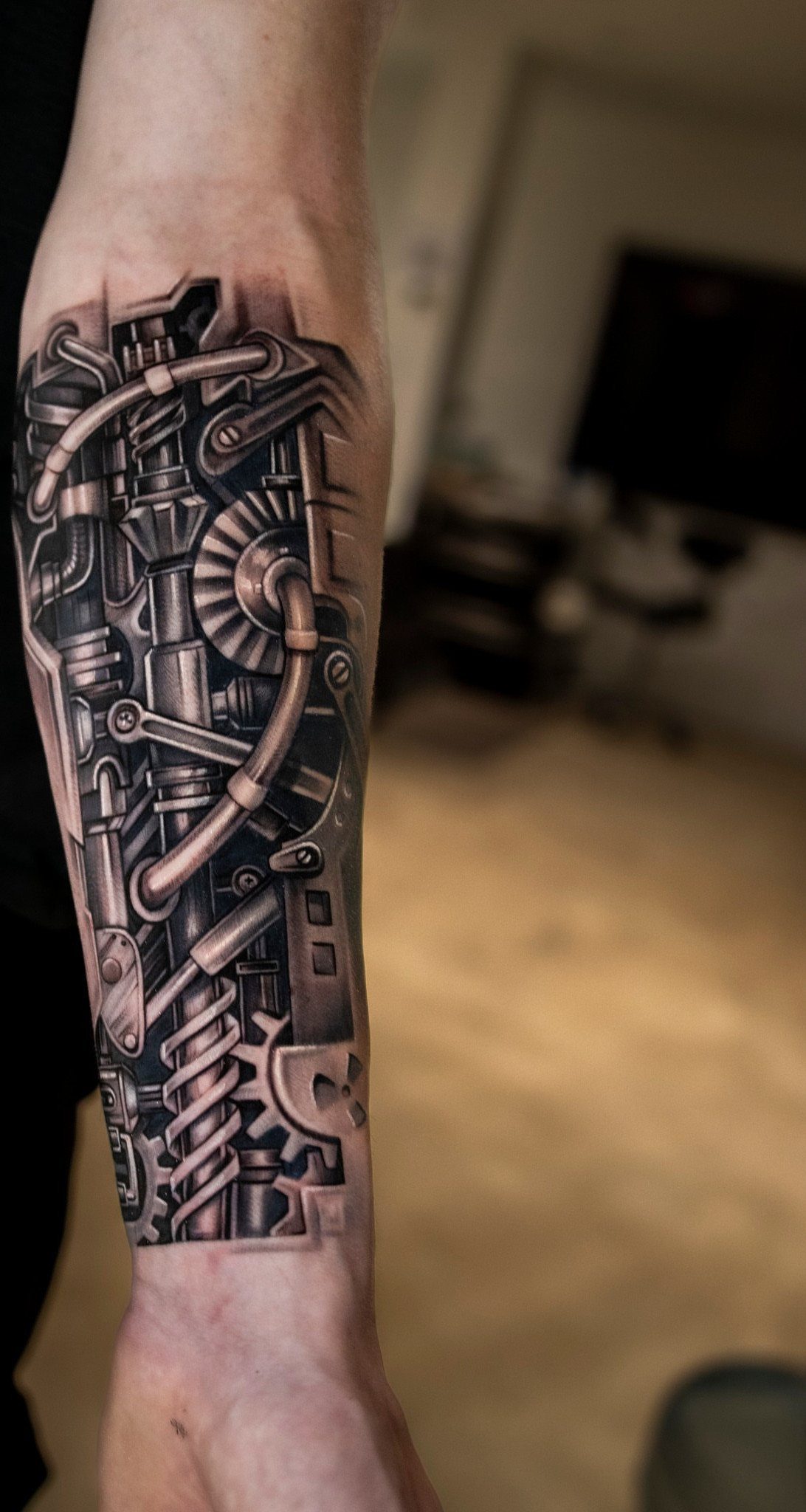 Biomechanical tattoo on a man's forearm featuring detailed metallic gears and pipes.