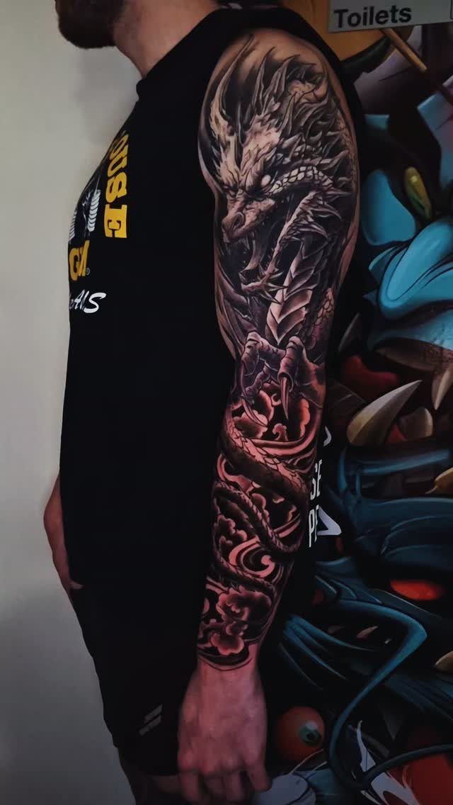 Detailed black and grey dragon sleeve tattoo on a man's arm.